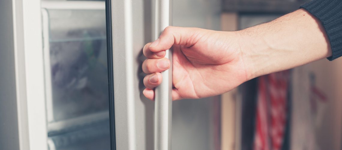The hand of a young man is opening a freezer door